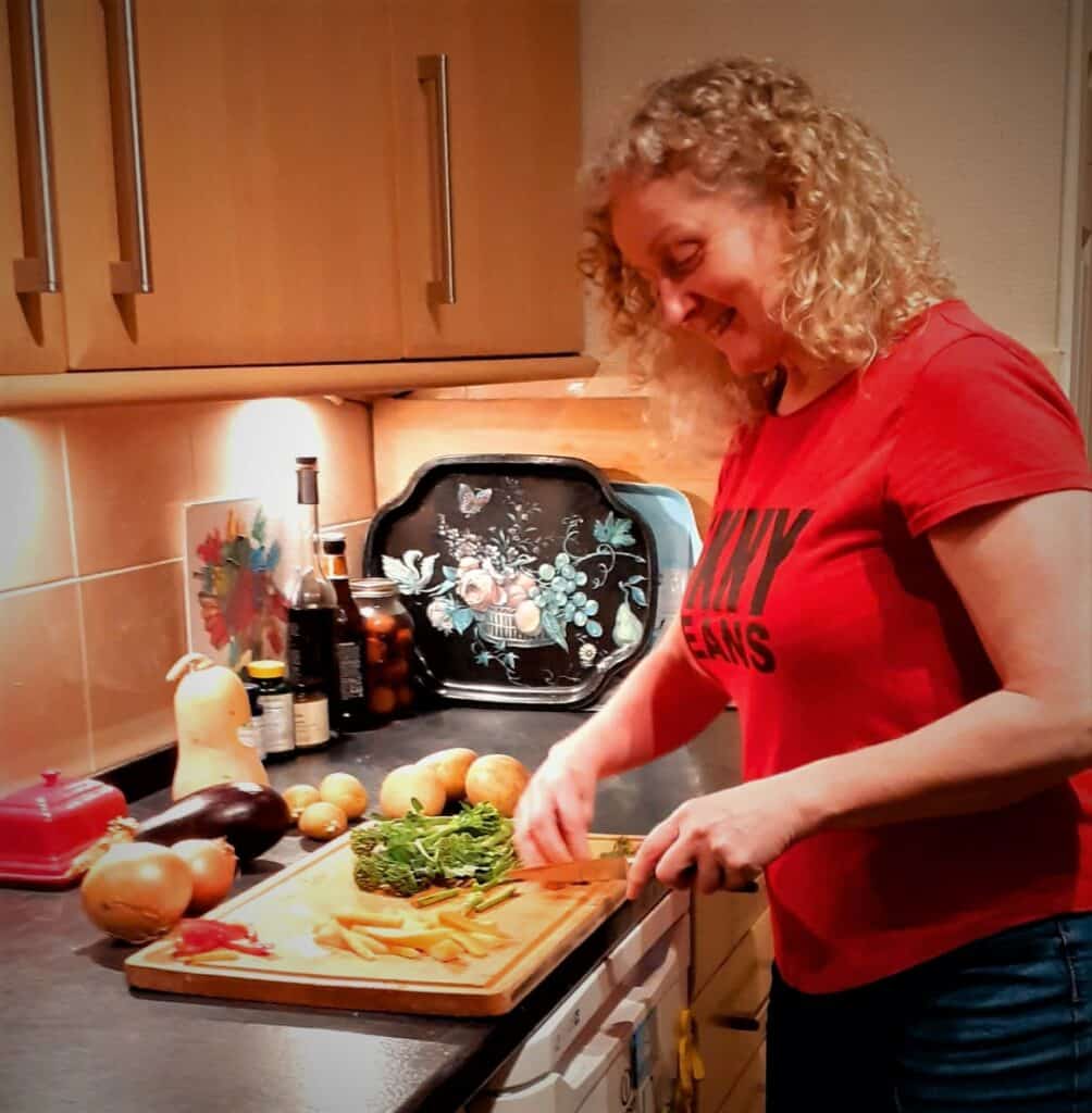 A woman chopping fresh vegetables in a cozy kitchen, showcasing the practical side of nutrition coaching in Leicester, focusing on healthy meal preparation for a balanced diet.